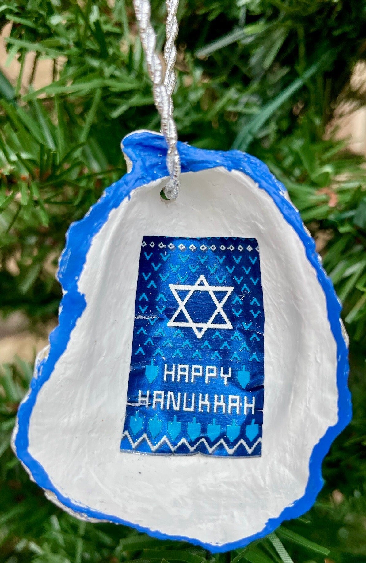 May include: A blue and white ornament shaped like a seashell with a blue and white Star of David and the text 'HAPPY HANUKKAH'.