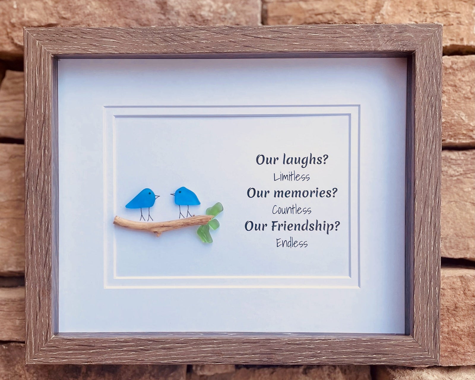 Framed picture with two blue birds on a branch and text about friendship against a wooden background