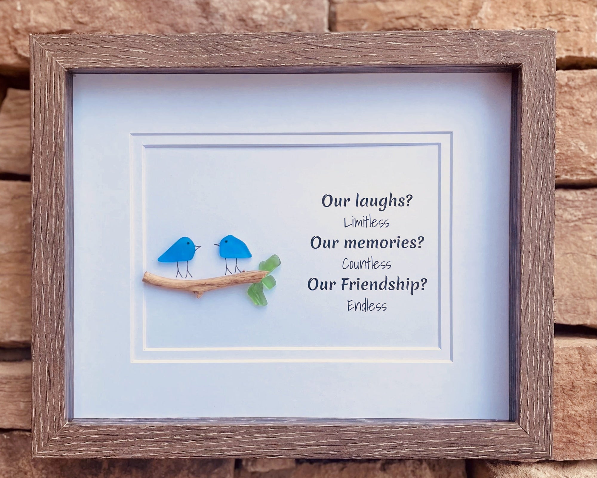 Framed picture with two blue birds on a branch and text about friendship against a wooden background
